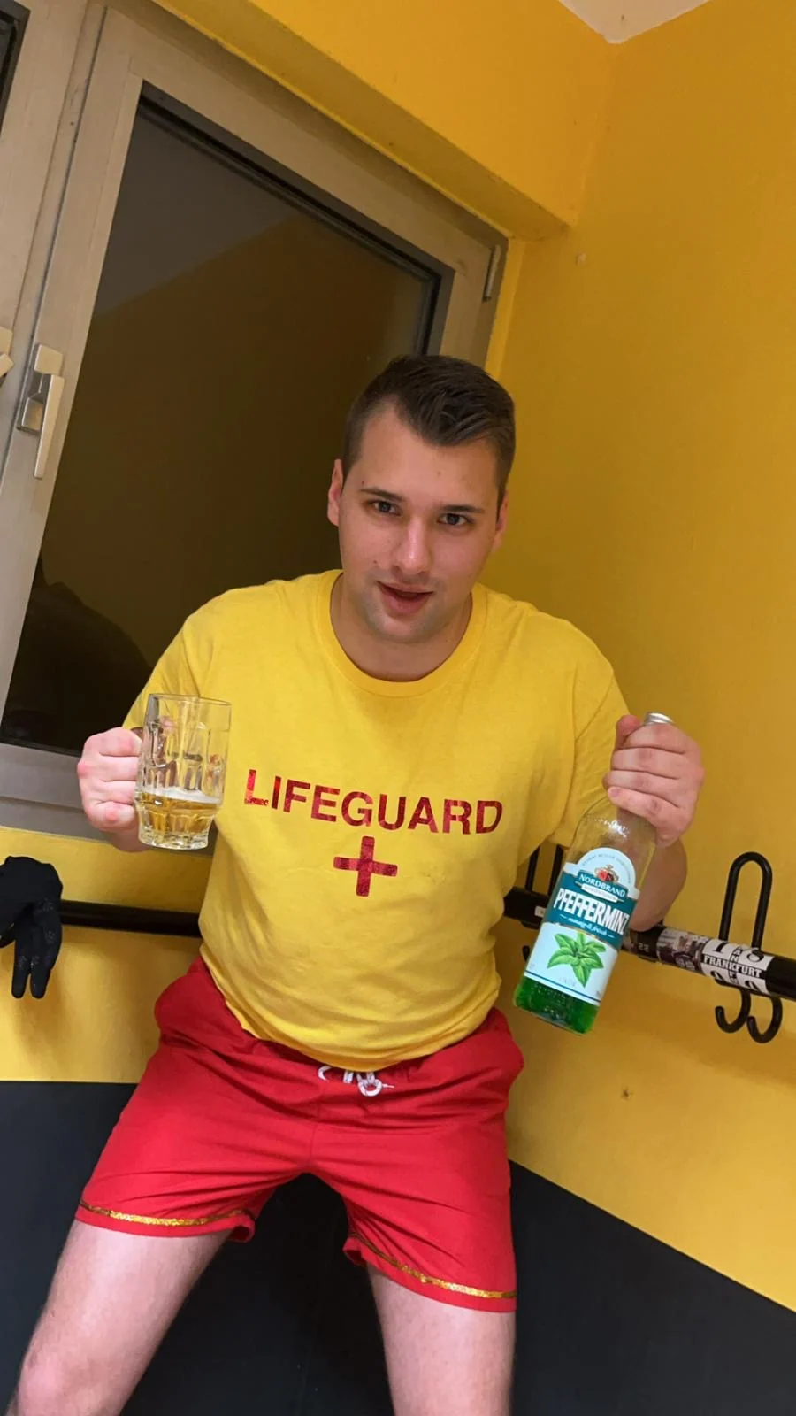 Ein Gruppenmitglied in gelbem Lifeguard-Shirt und roten Shorts posiert mit Getränken.